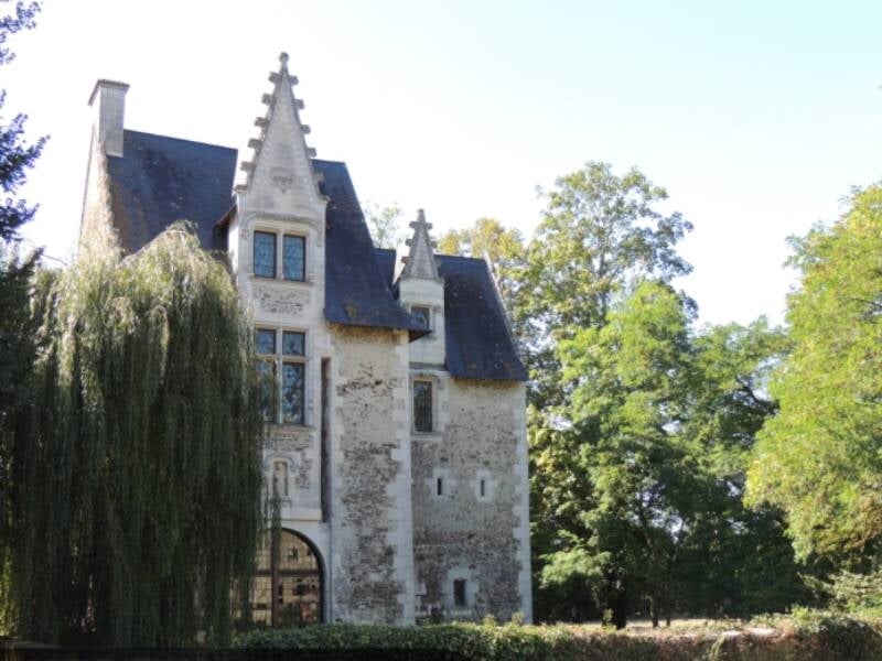 Vue d'un vieux manoir en pierre avec un toit en ardoise et un grand saule pleureur à gauche