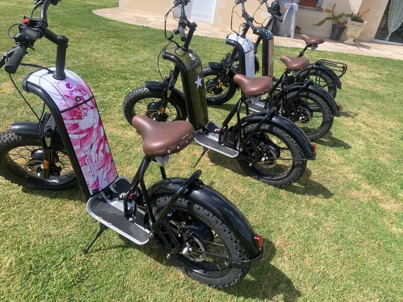 Quatre trottinettes électriques noires avec selle marron alignées sur une pelouse verte