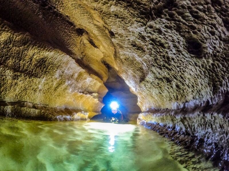 Plongeur avec lampe frontale nageant dans une étroite galerie sous-marine aux parois rocheuses.