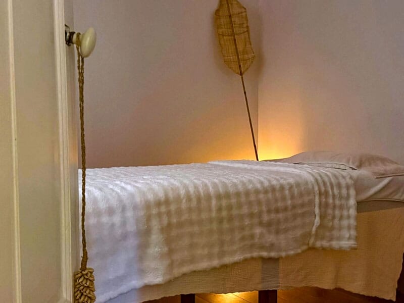 Table de massage avec couverture blanche dans une pièce calme éclairée par une lumière douce et chaleureuse.