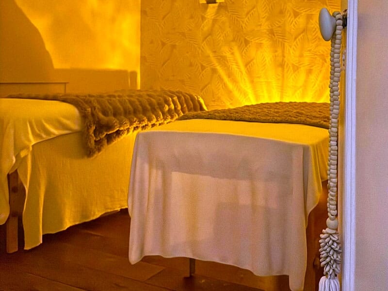 Deux tables de massage avec couvertures dans une pièce aux murs décorés d'un motif végétal jaune.