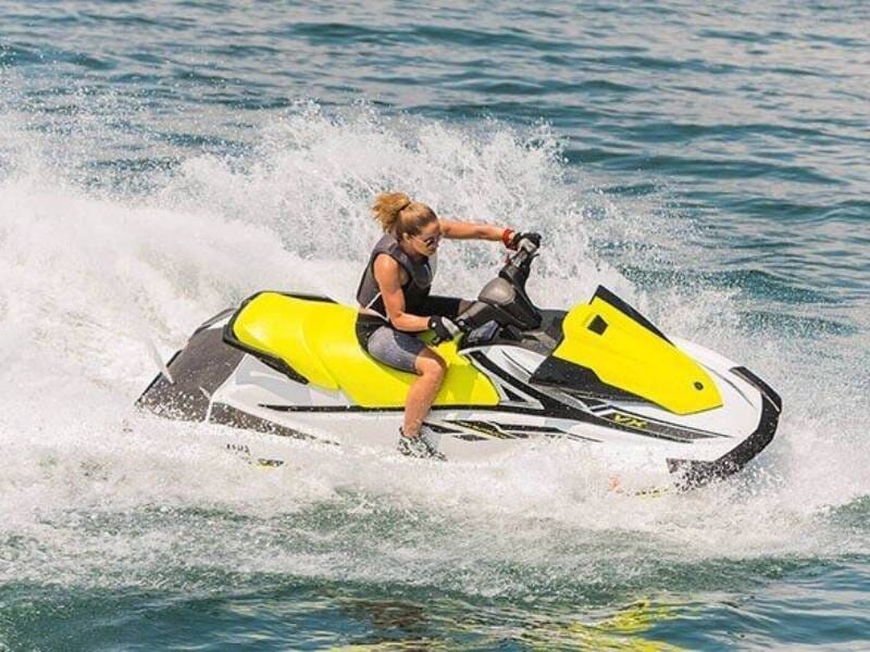 Femme en gilet de sauvetage noir conduisant un jet ski blanc et jaune sur une eau agitée avec éclaboussures, lors d'une randonnée à Pornic.