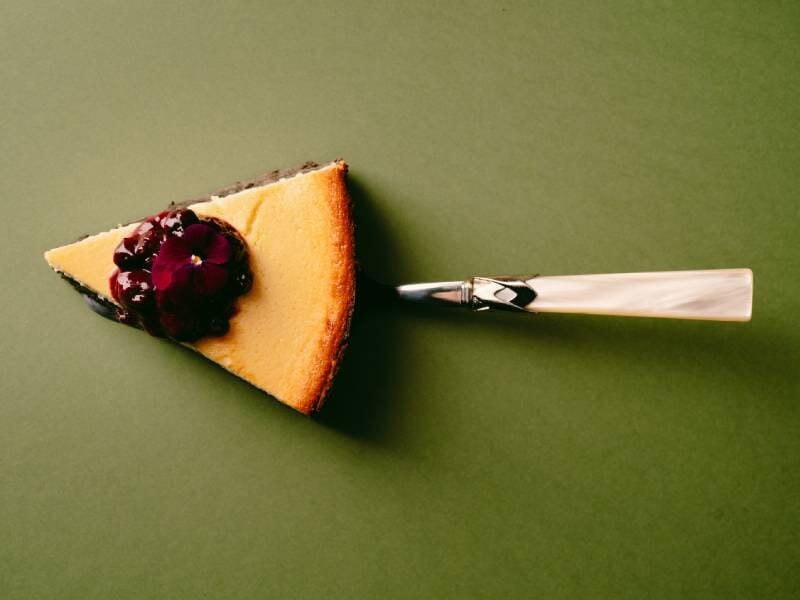 Part de gâteau décorée de fruits rouges, posée sur une pelle à tarte sur un fond vert uni, réalisée lors d'un cours de cuisine près d'Avignon.