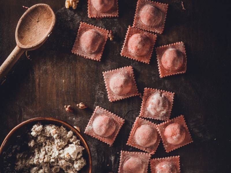 Raviolis frais posés sur une table en bois avec une cuillère en bois et de la farce à côté.