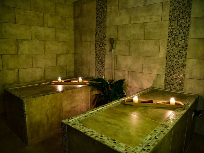 Deux tables de massage en pierre avec bougies allumées, ambiance tamisée et décor zen.