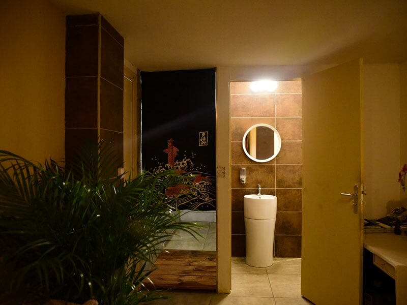 Entrée d'une salle de spa avec plantes, miroir rond et lumière douce, ambiance chaleureuse.