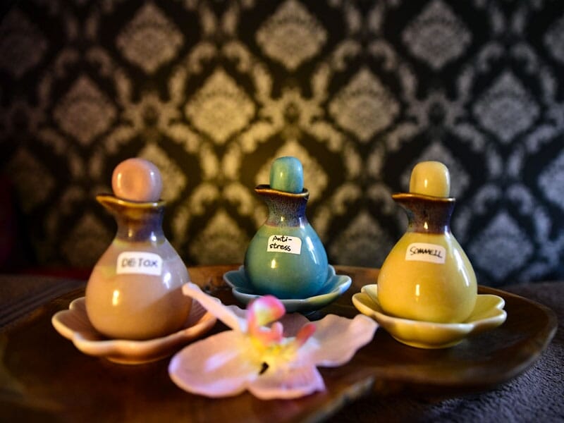 Trois flacons d'huiles essentielles colorées posés sur un plateau en bois avec une fleur d'orchidée.