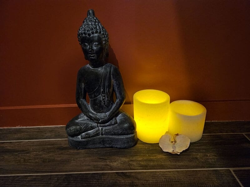 Statue de Bouddha assis à côté de deux bougies jaunes allumées sur un sol en bois.