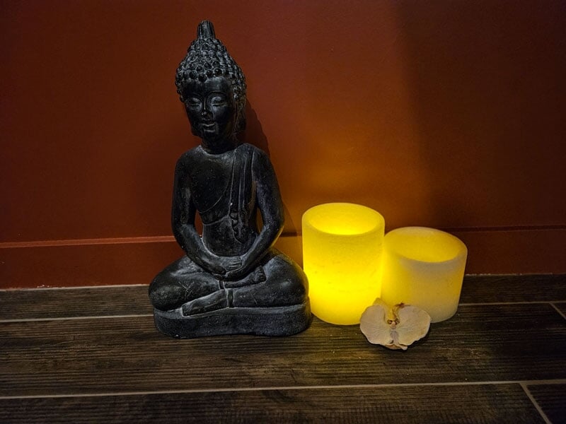 Statue de Bouddha assis à côté de deux bougies jaunes allumées sur un sol en bois.