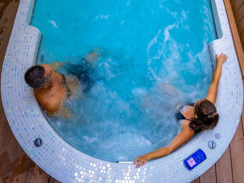 Deux personnes profitent d'un bain à remous dans un spa avec eau claire et jets massants actifs.
