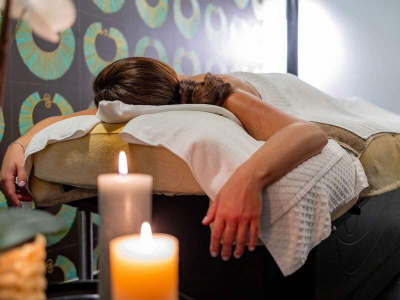 Une femme allongée sur une table de massage, ambiance relaxante avec bougie allumée au premier plan.