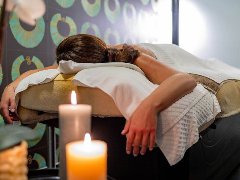 Une femme allongée sur une table de massage, ambiance relaxante avec bougie allumée au premier plan.