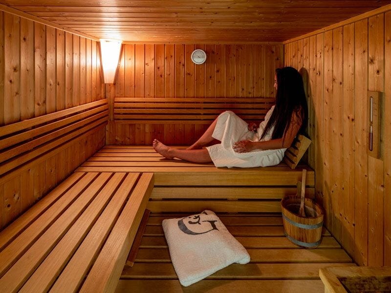 Une femme assise dans un sauna en bois, enveloppée dans une serviette blanche, profitant de la chaleur.