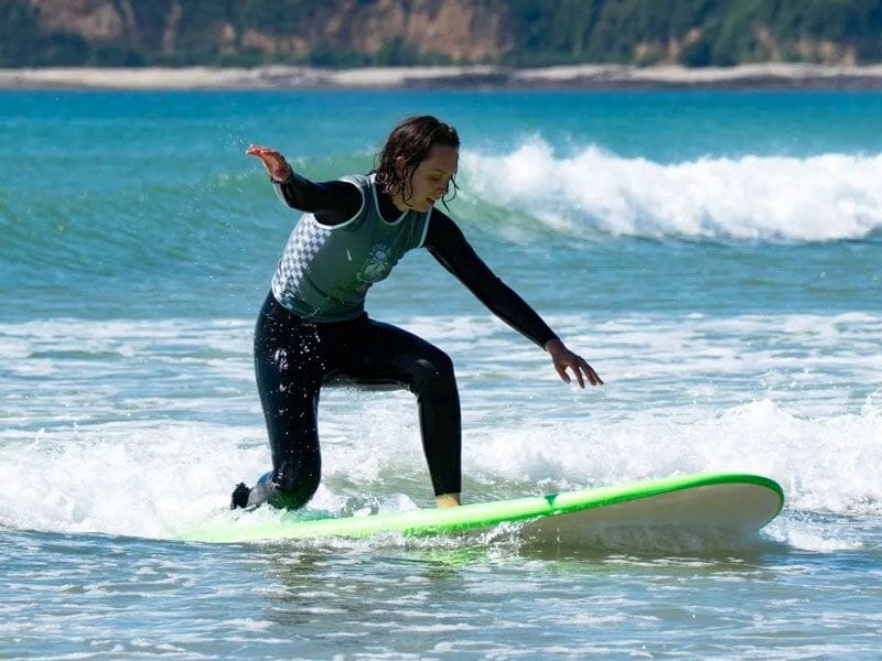 Jeune surfeur debout sur une planche verte, équilibre en train de glisser sur une petite vague à la plage.