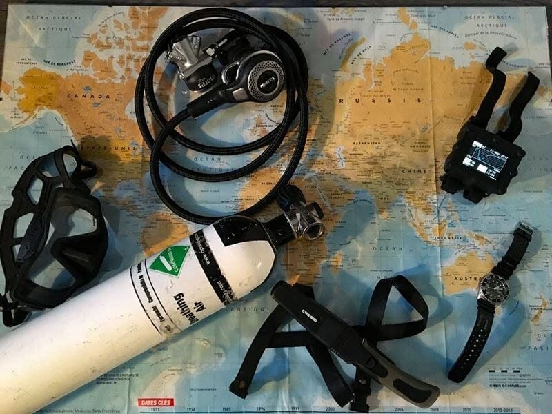Matériel de plongée sous-marine posé sur une carte du monde, incluant masque, bouteille et montre étanche.