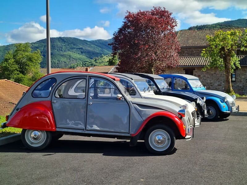 Cinq voitures Citroën 2CV de différentes couleurs garées en rangée sur un parking sous un ciel bleu.