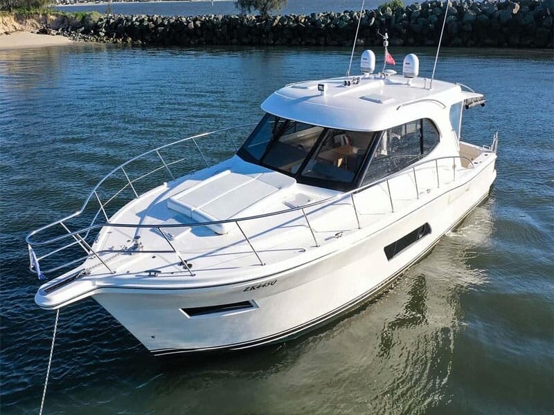 Bateau blanc moderne amarré sur l'eau calme avec une digue en arrière-plan sous un ciel clair.
