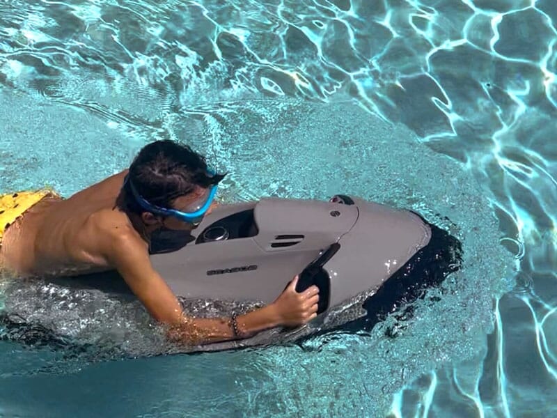 Enfant avec masque de plongée jouant avec un scooter sous-marin dans une piscine claire.
