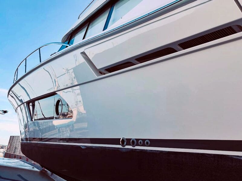Gros plan sur la coque blanche brillante d'un bateau avec des détails de fenêtres et aérations.