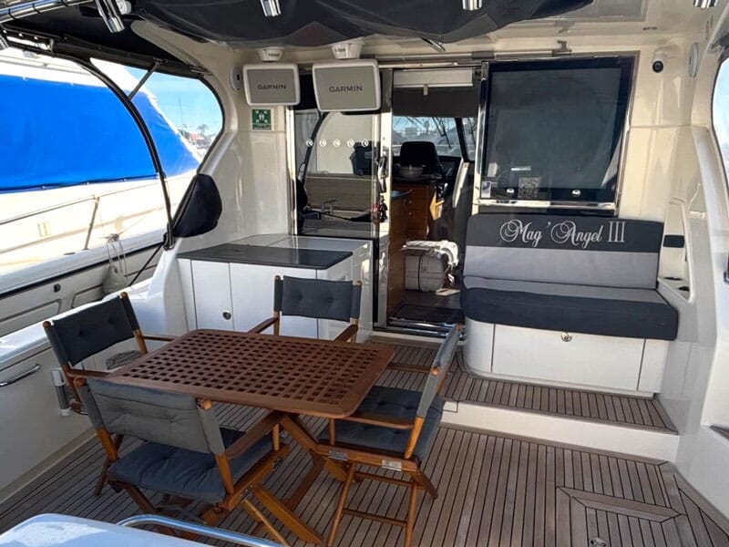 Intérieur d'un bateau avec table en bois, chaises pliantes et équipements électroniques visibles.