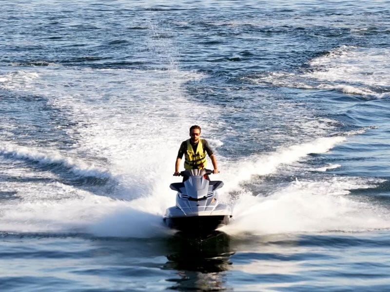 Personne conduisant un jetski sur une mer calme avec éclaboussures d'eau autour du véhicule en mouvement rapide.