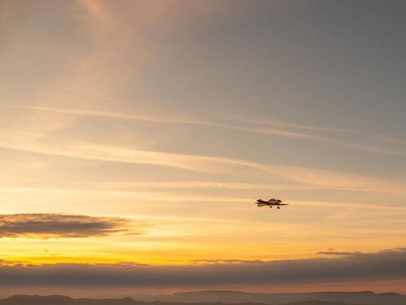 Avion de voltige volant au loin dans un ciel aux couleurs chaudes du coucher de soleil.
