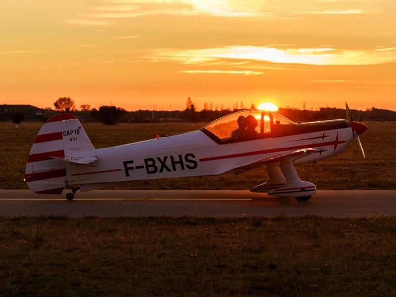 Avion de voltige blanc et rouge au sol avec le soleil couchant en arrière-plan.