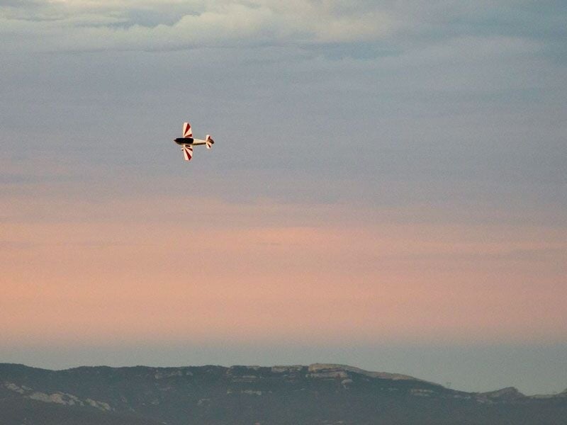 Avion de voltige volant au-dessus d'un paysage montagneux sous un ciel aux teintes rosées.