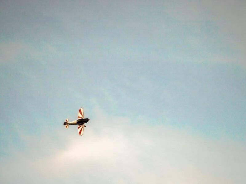 Avion de voltige en vol avec un ciel bleu clair et quelques nuages légers en arrière-plan.