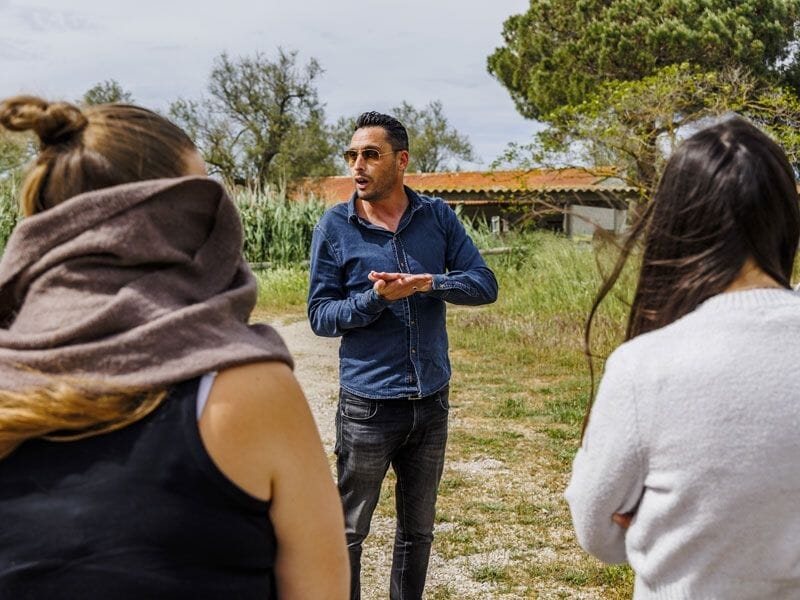 Un homme explique un stage de pilotage 4x4 à deux femmes dans un cadre naturel ensoleillé et verdoyant.