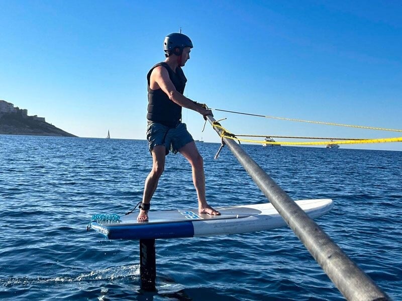 Homme en casque pratiquant le wakeboard sur une planche à foil sur une mer calme avec un ciel bleu clair.