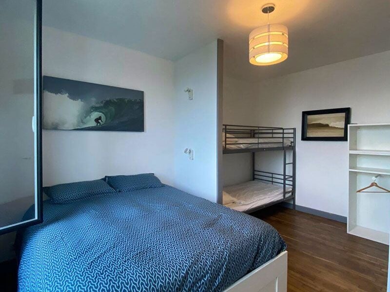 Chambre avec lit double, lits superposés, parquet en bois et décorations murales sur le thème du surf.
