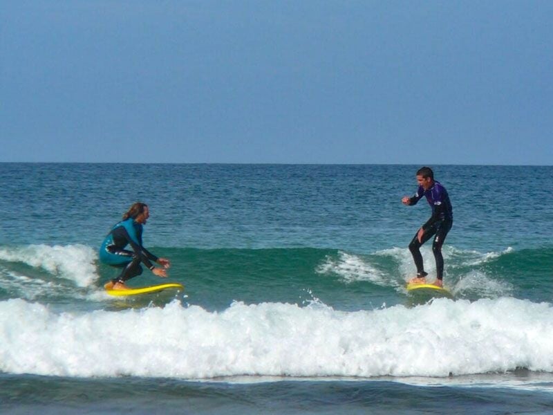 Deux surfeurs debout sur leurs planches, glissant sur une petite vague dans une mer calme.