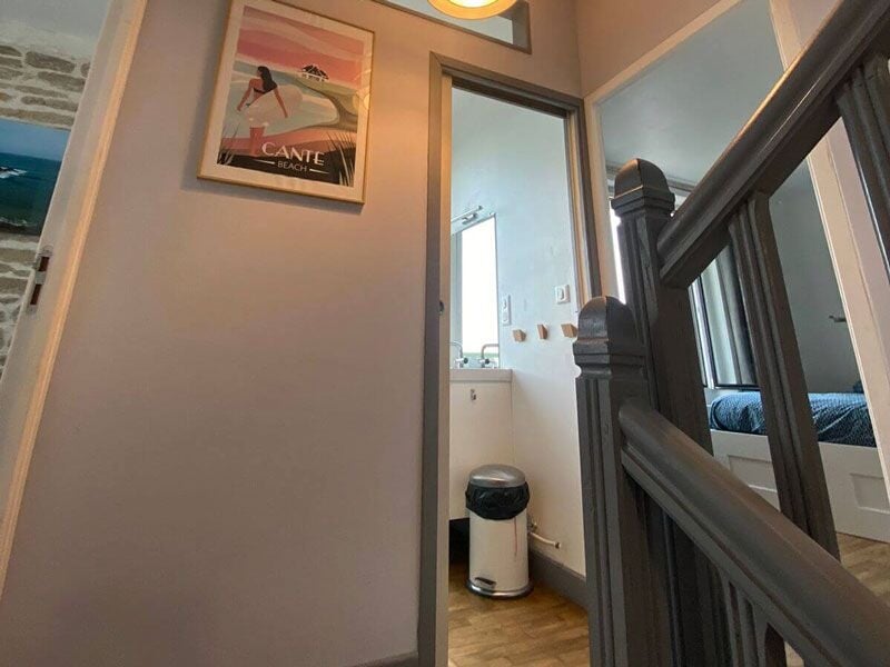 Escalier intérieur avec murs clairs, cadre photo et porte ouverte menant à une autre pièce.