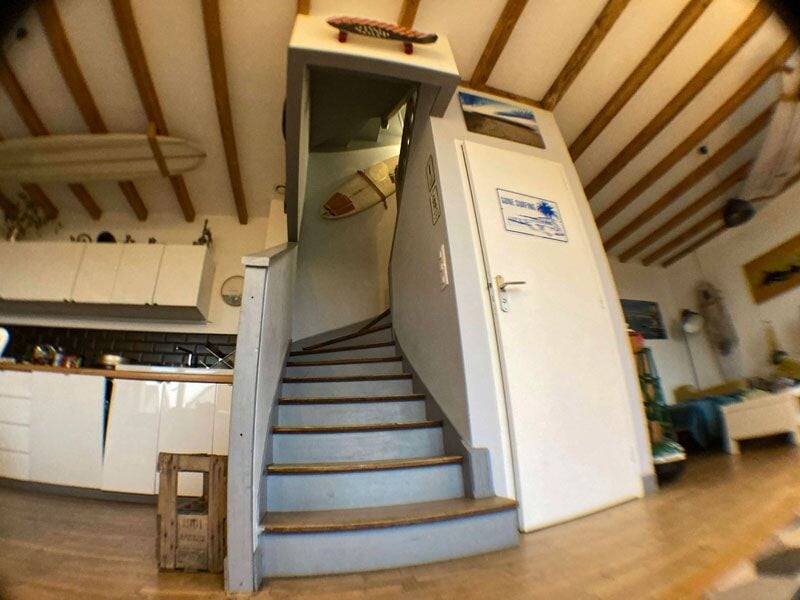 Escalier en colimaçon dans une maison avec poutres apparentes et cuisine moderne visible au fond.