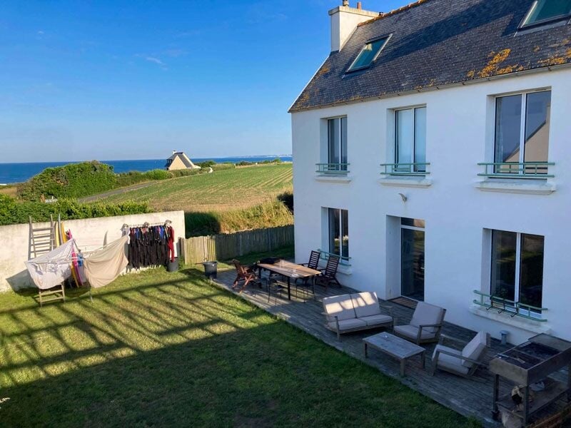 Vue arrière d'une maison avec jardin, mobilier d'extérieur et étendoir à linge sous un ciel bleu clair.