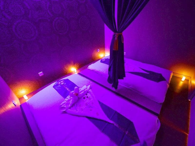 Chambre de spa avec deux lits de massage, éclairage violet et ambiance relaxante pour soins bien-être.
