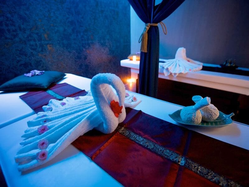Tables de massage décorées avec serviettes pliées en forme de cygnes et ambiance spa apaisante.