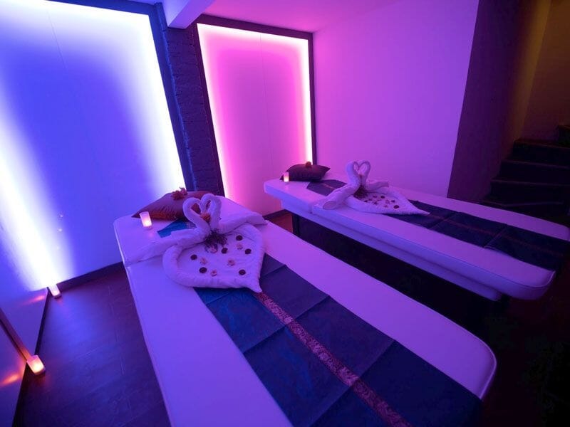 Espace spa avec deux tables de massage, éclairage rose et violet, décor moderne et relaxant.