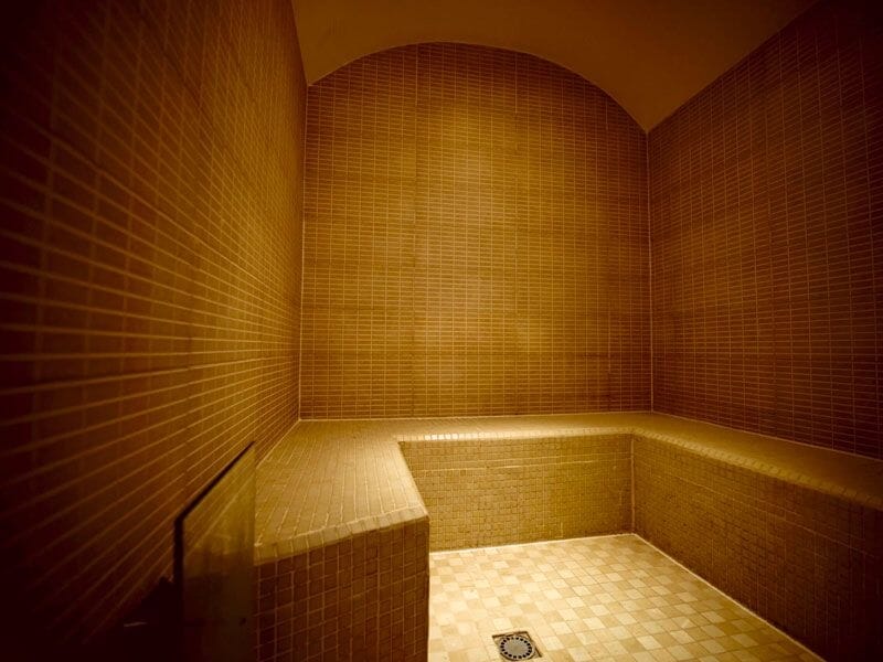Hammam avec murs carrelés beige, banquette en angle et lumière chaude pour détente et bien-être.