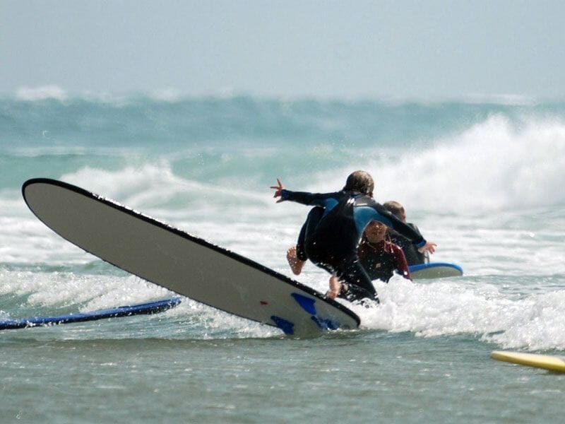 Deux enfants en combinaison de surf apprenant à surfer sur une planche blanche dans les vagues de l'océan.