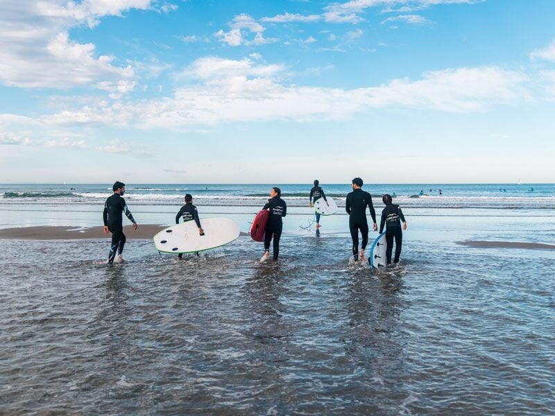 Groupe de surfeurs marchant vers l'océan avec leurs planches sous un ciel partiellement nuageux à Anglet.