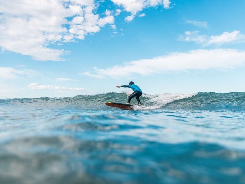 Surfeur en combinaison bleue glissant sur une vague bleue claire avec un ciel nuageux en arrière-plan.