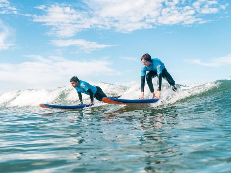 Deux jeunes surfeurs debout sur leurs planches, surfant côte à côte sur une vague à Anglet.