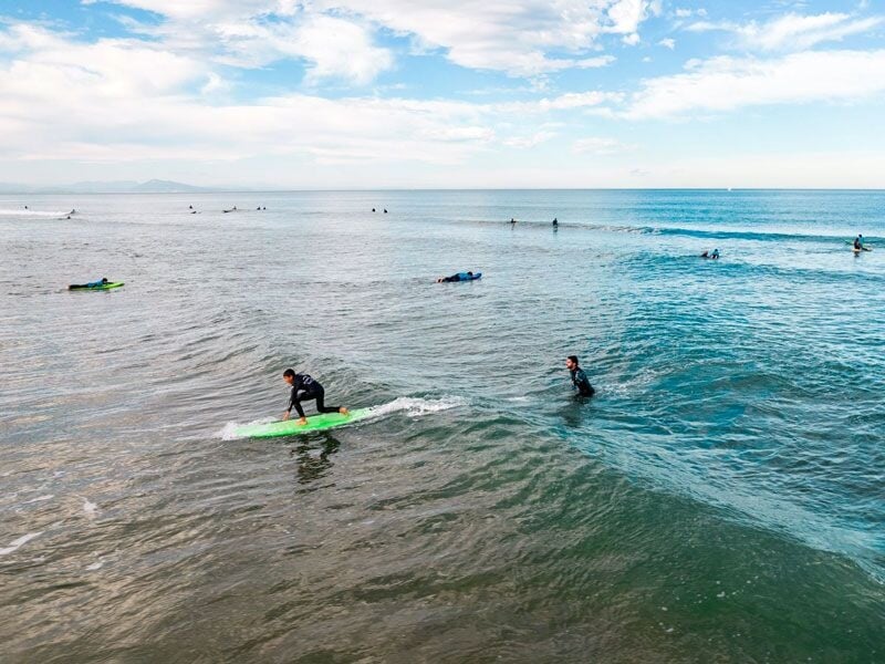 Surfeur debout sur une planche verte, glissant sur une petite vague dans une mer calme à Anglet.