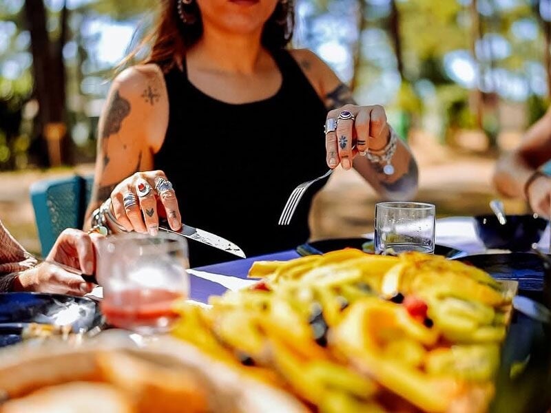 Personne assise à une table en extérieur, mangeant un plat de frites avec des boissons sur la table.