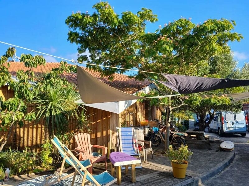 Espace extérieur avec des chaises longues, des plantes et des voiles d'ombrage sous un ciel bleu clair.