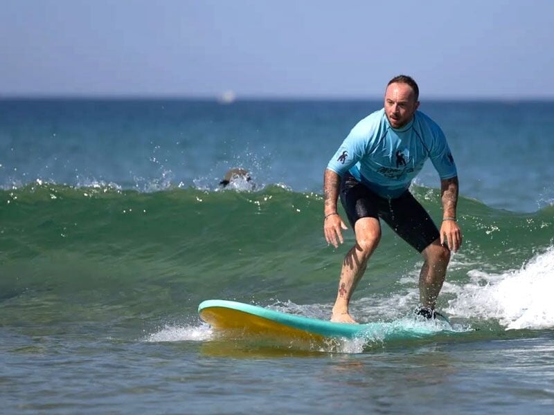 Homme en combinaison de surf debout sur une planche, surfant une petite vague dans l'océan.