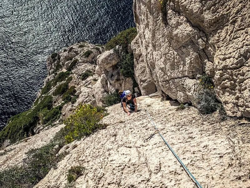 Grimpeur en casque bleu escaladant une falaise rocheuse au-dessus de la mer Méditerranée à Marseille.