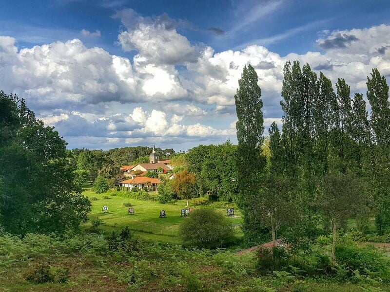 Vue panoramique d'un village entouré d'arbres verts sous un ciel nuageux avec des cibles de tir à l'arc dans un champ.